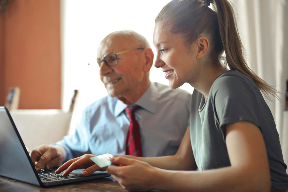old man and young women sat in front of laptop paying for goods with car